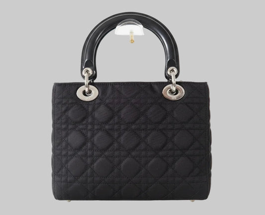 Black quilted handbag with silver hardware on a gray background