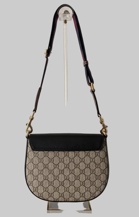 Gucci handbag with GG front and black top section on a stand against a light gray background