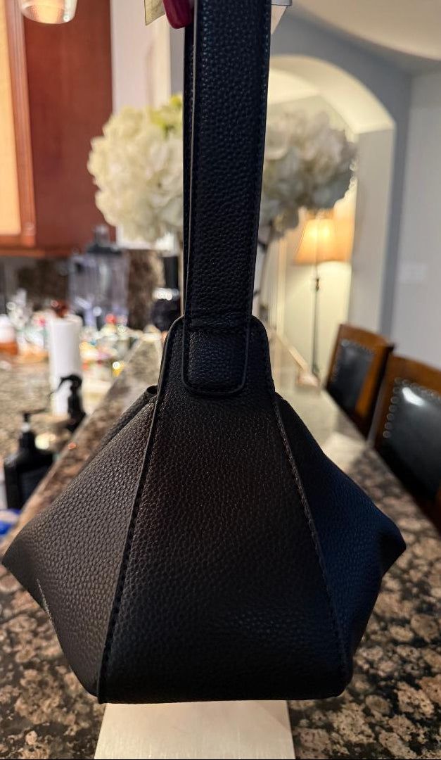 A black pebbled leather shoulder bag with a structured, geometric triangular body and a single strap, shown hanging on a kitchen counter.