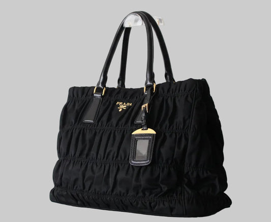 Black Prada handbag with gold hardware and luggage tag ruched design on a gray background
