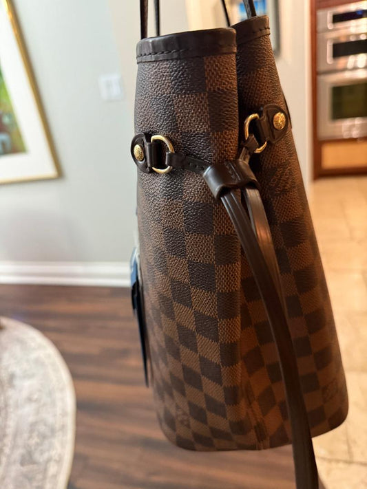 Brown checkered handbag with gold accents on a wooden floor.