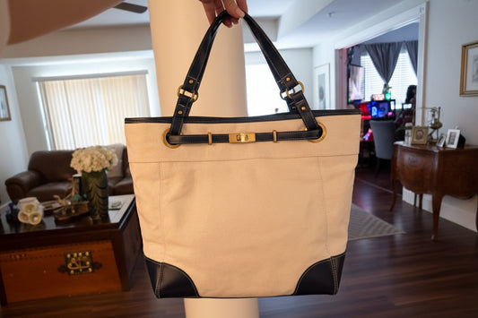 Beige tote bag with black accents held by a person indoors.