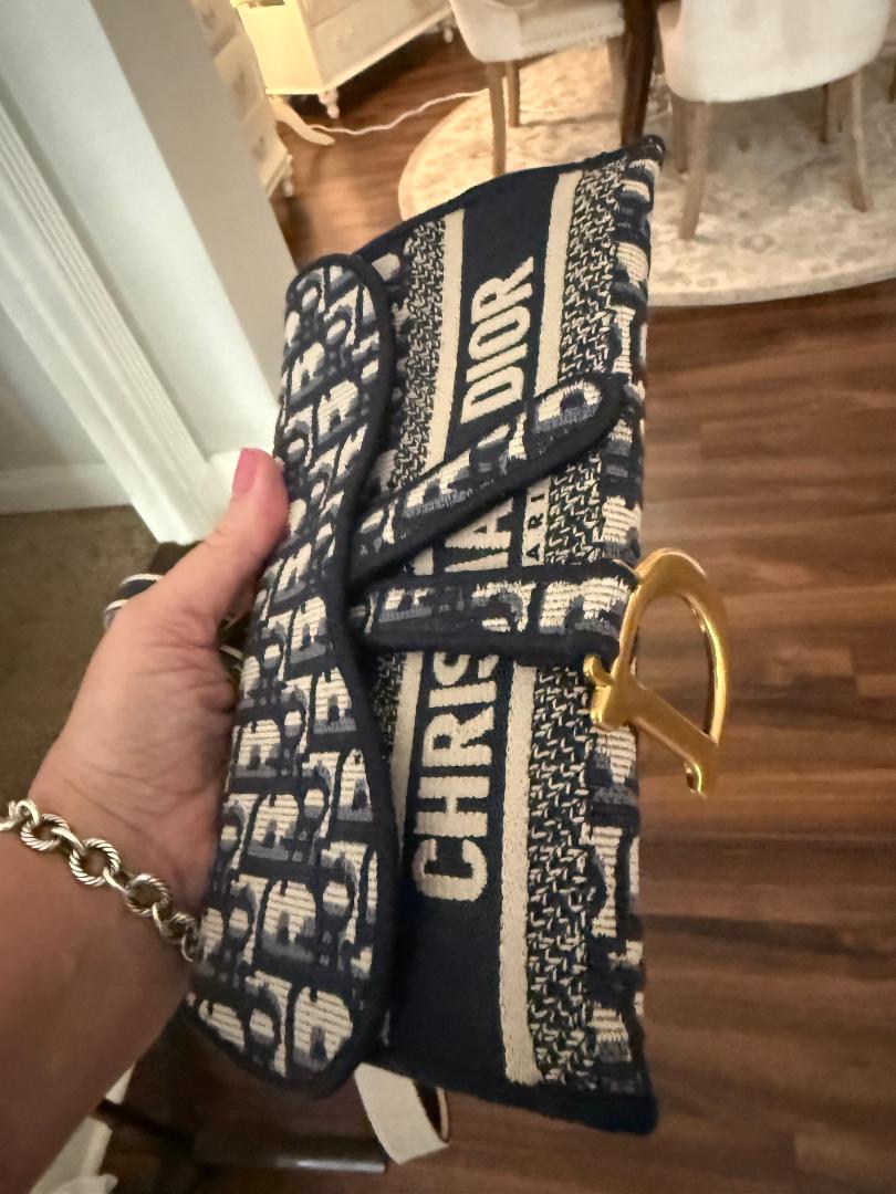 Hand holding a Christian Dior handbag with a gold clasp in an indoor setting.
