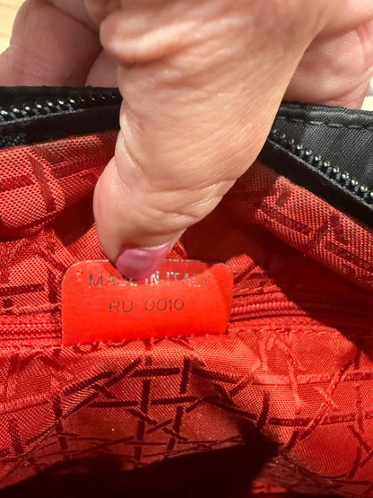 Close-up of a black lady Dior with red inside bag with a visible brand label.