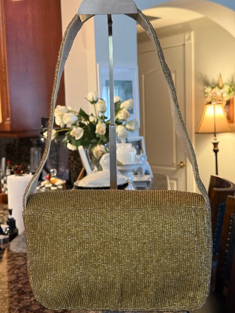 A sparkly gold shoulder bag with a textured, shimmering finish, hanging on a metal display stand in a home interior setting.