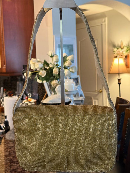 A sparkly gold shoulder bag with a textured, shimmering finish, hanging on a metal display stand in a home interior setting.