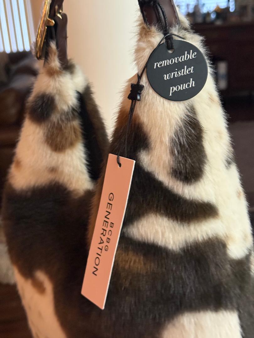 A close-up of a fur accessory with a brown, black, and cream mottled pattern, featuring a black circular tag that reads 'removable wristlet pouch' and a peach-colored hangtag with the brand name 'BONGA GENERATION'.