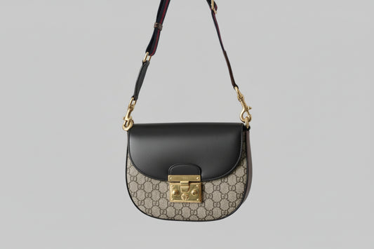 Gucci handbag with black leather flap and gold hardware on a gray background