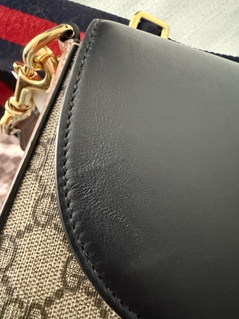 Close-up of a black leather handbag with gold hardware on a textured surface.