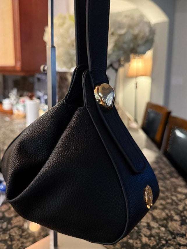 A black pebbled leather shoulder bag with gold-tone hardware, hanging on a display stand in a kitchen environment.