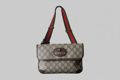 Gucci handbag with a monogram pattern and red and green strap on a gray background