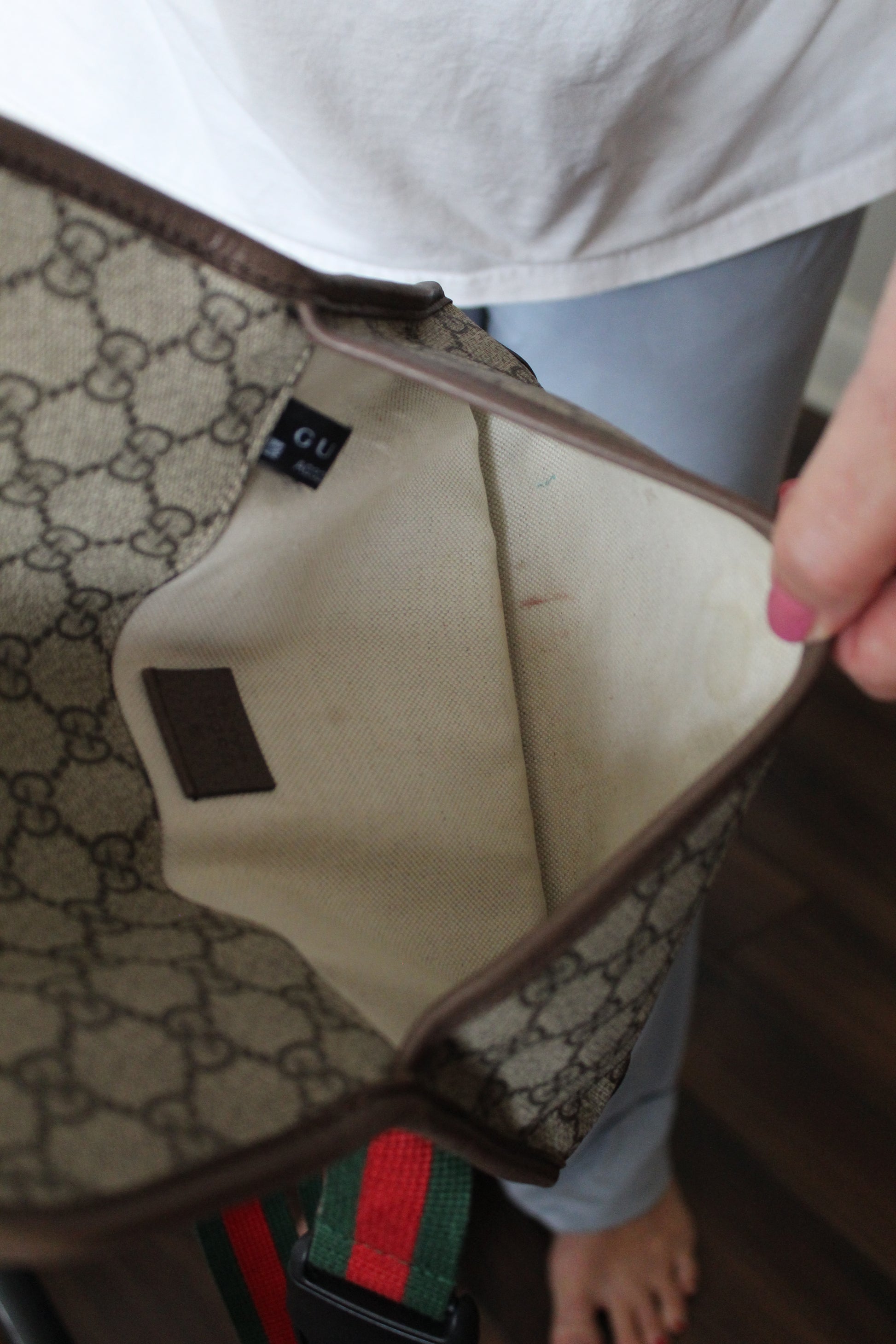 Close-up of a hand holding a beige clutch with a patterned interior, sitting on a surface.