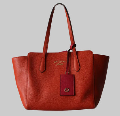 Gucci orange leather handbag with a visible brand tag on a gray background