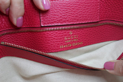 Close-up of a orange/pink Gucci handbag with a person's hand holding it.