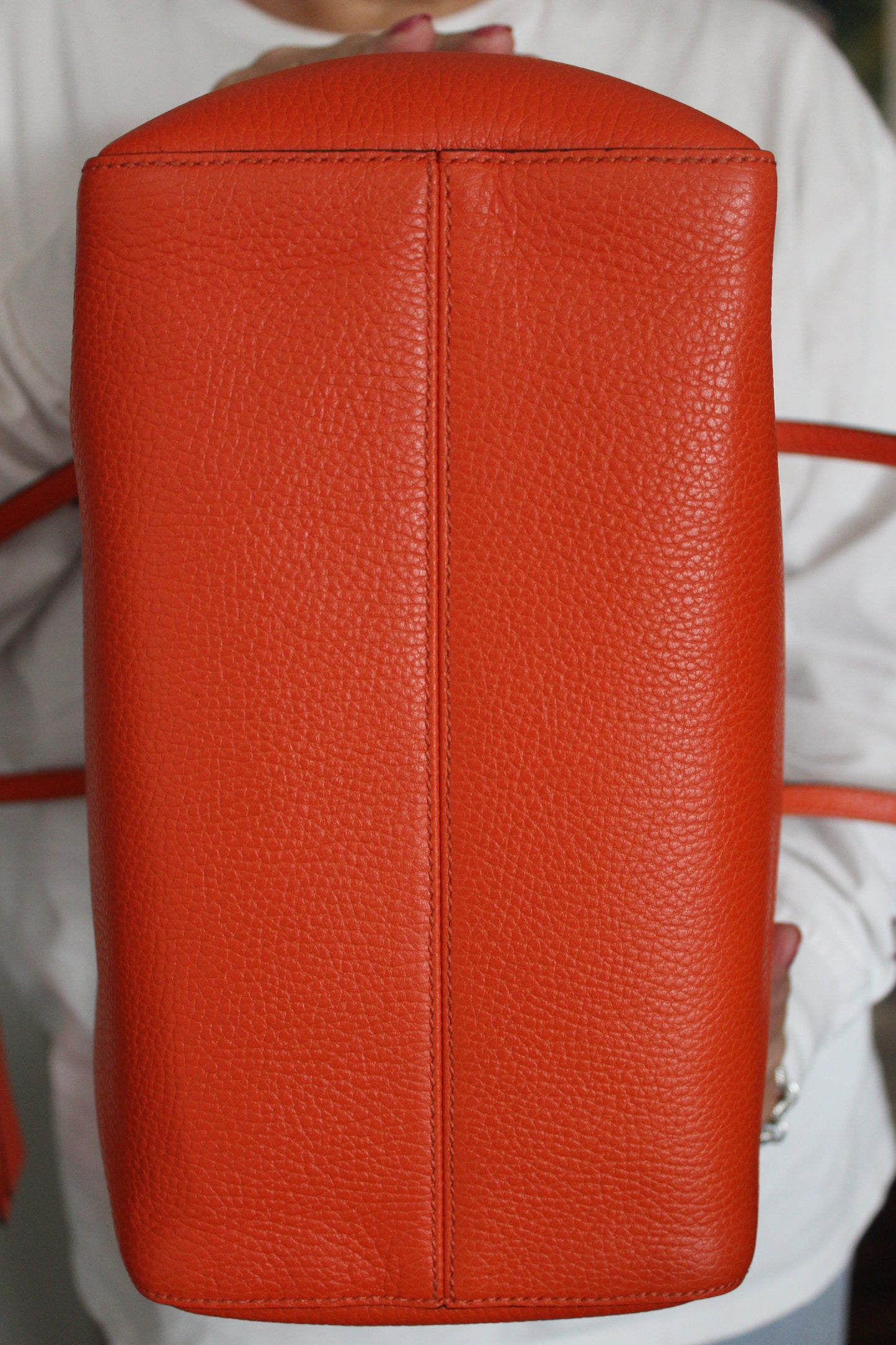 Gucci orange bottom handbag held by a person wearing a white shirt.