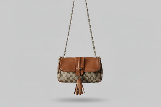 Gucci Brown leather handbag with a chain detail and tassel on a gray background