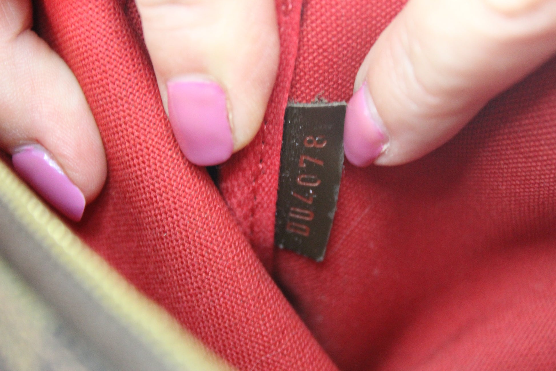 Close-up of a red fabric with a label and pink nail polish.