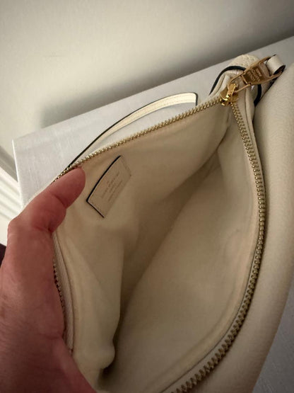 Close-up of a beige handbag with a gold zipper, held by a hand.
