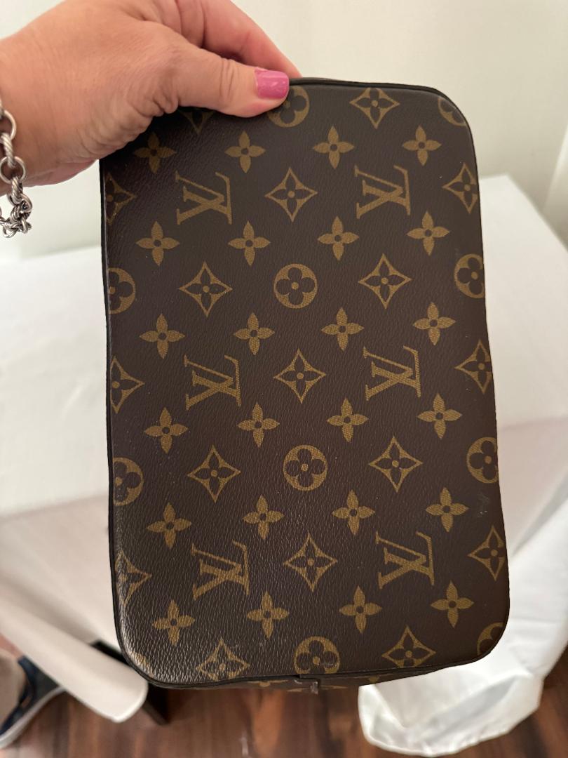Louis Vuitton monogram patterned pouch held by a hand with pink nail polish.