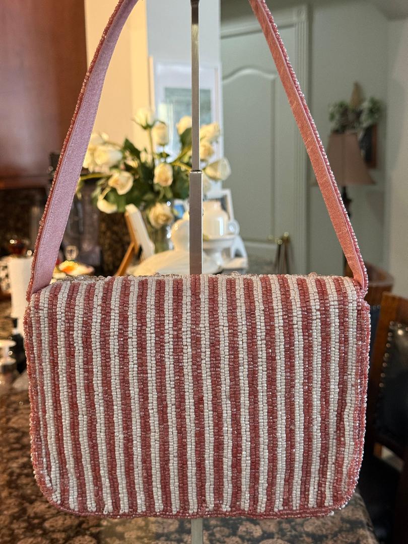 A pink and white vertically striped woven shoulder bag with a matching pink strap, displayed on a stand in a home interior setting.