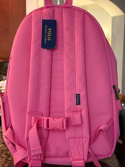 A pink Polo Ralph Lauren backpack shown from the back, featuring padded shoulder straps, a buckle closure, a zippered pocket on the right, and a blue brand hangtag.