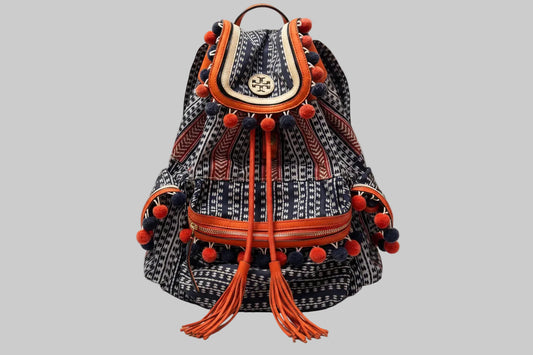 Patterned Tory Burch backpack with orange accents on a navy background with orange tassels