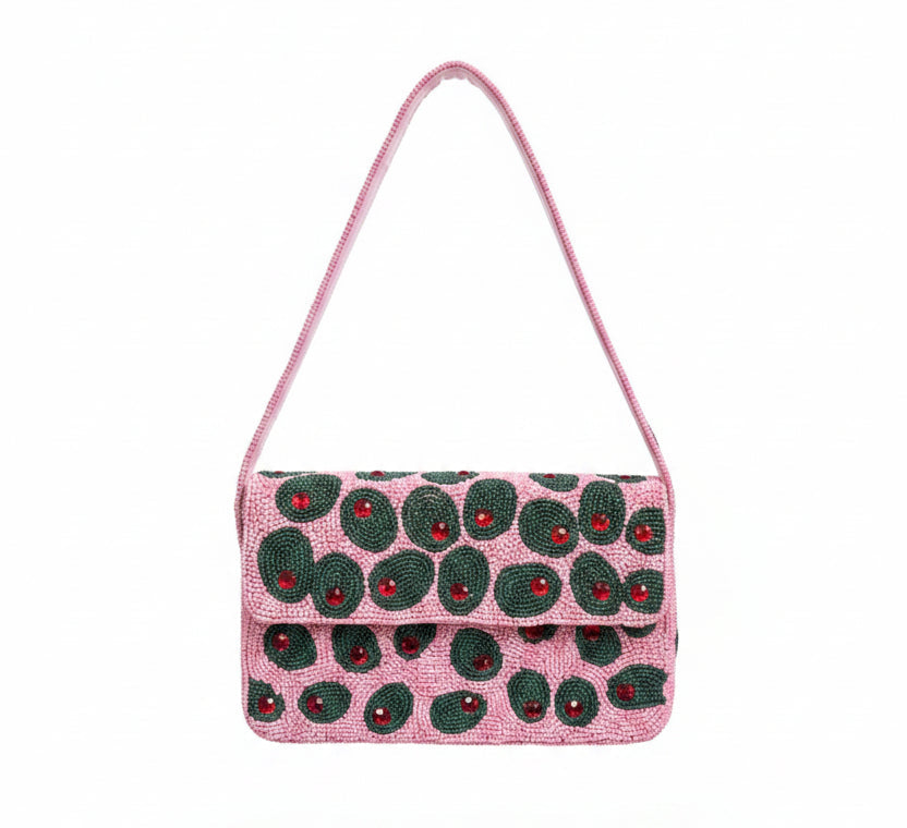 A pink beaded shoulder bag with a flap closure, decorated with a pattern of green olives. The bag has a thin pink strap and is shown against a plain white background with a soft drop shadow.
