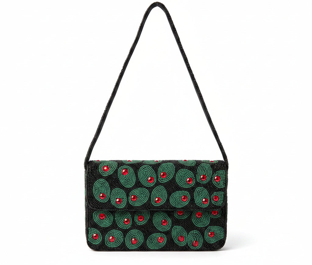 A black beaded shoulder bag with green olives and red center accents, hanging outdoors in front of green foliage and white flowers.