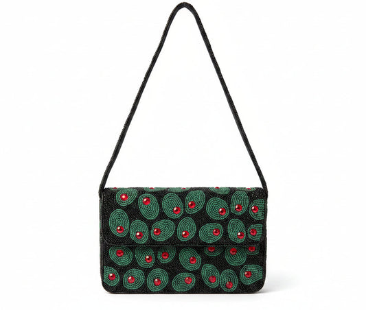 A black beaded shoulder bag with green olives and red center accents, hanging outdoors in front of green foliage and white flowers.