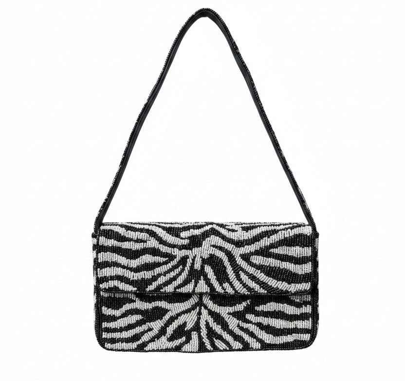 A black beaded and white zebra-print shoulder bag with a black strap, set against a background of reddish-purple and green foliage.