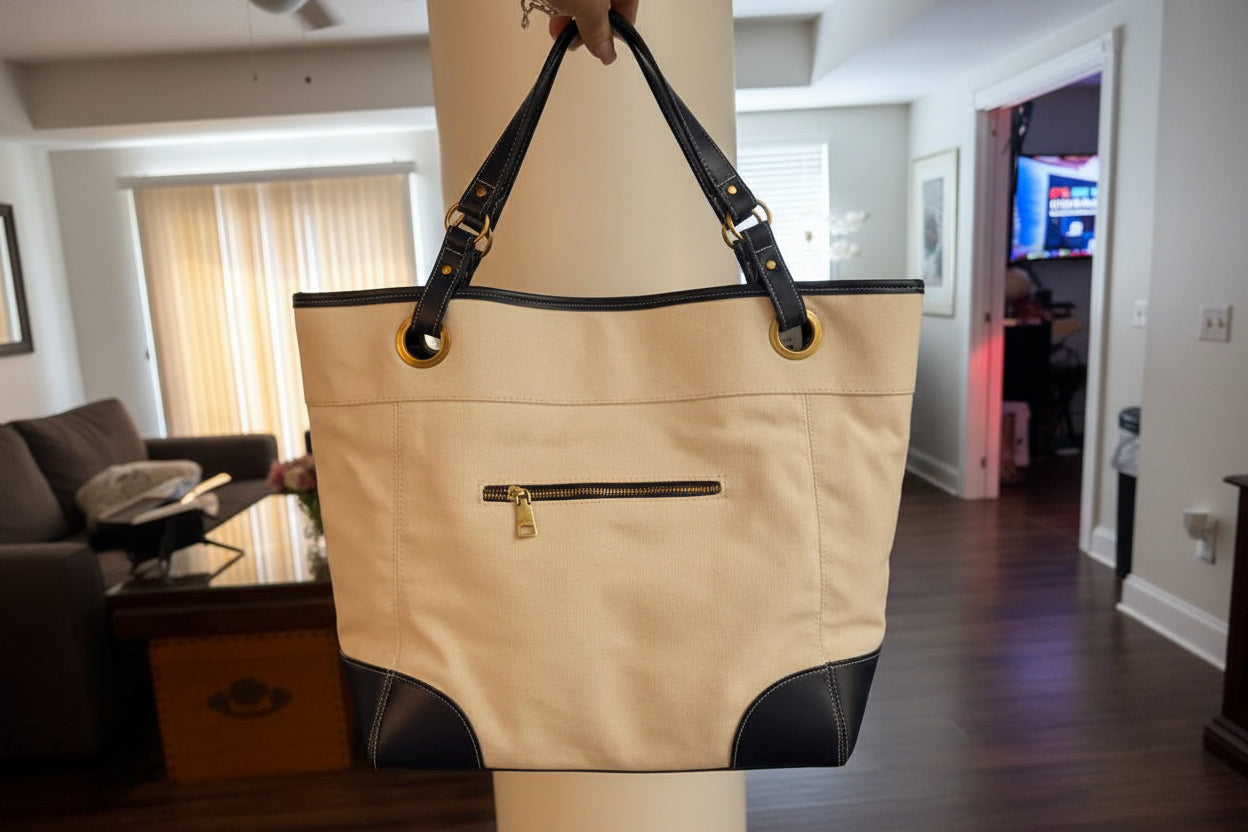 Beige handbag with black accents held by a person on a mannequin.