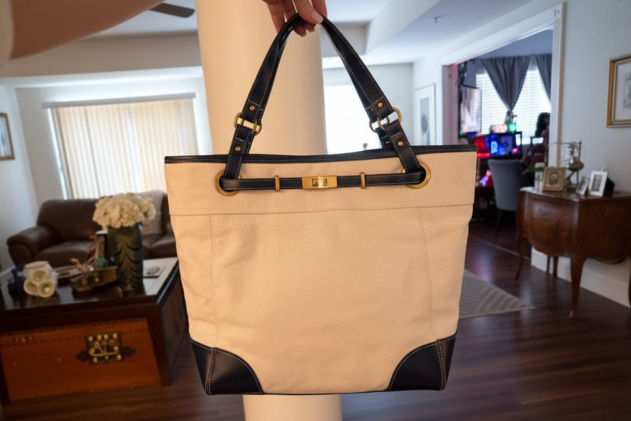 Beige tote bag with black accents held by a person indoors.